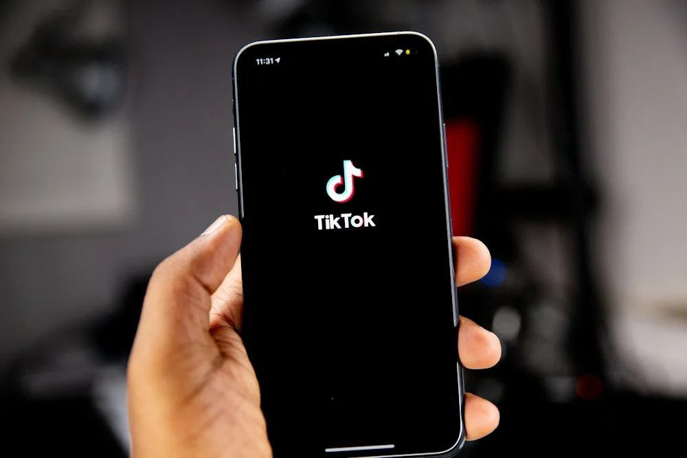Hand holding a phone with the TikTok logo, guide to buy TikTok comments