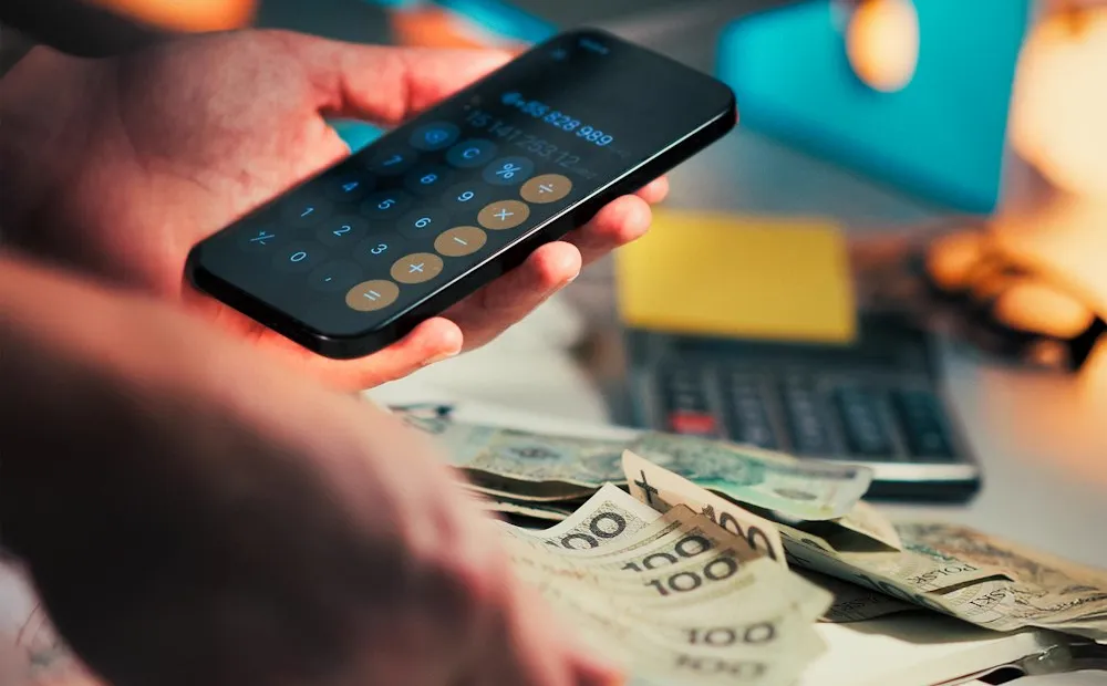 Person checking a calculator app next to cash: cost to buy Instagram followers