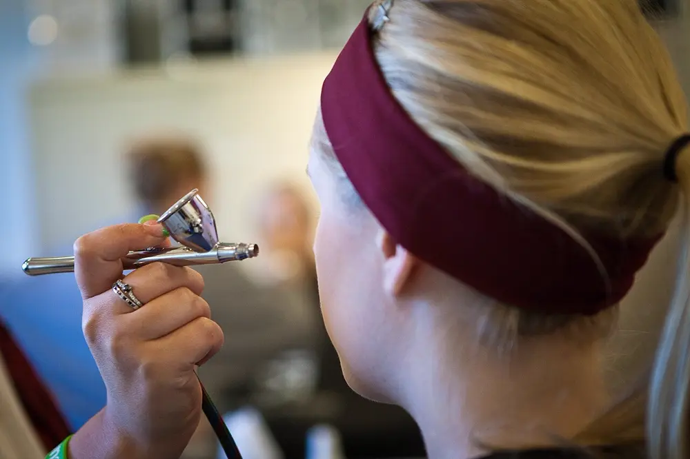 A makeup artist using an airbrush gun to apply bridal makeup, illustrating the airbrush technique bridal artists use for long-wear wedding day looks