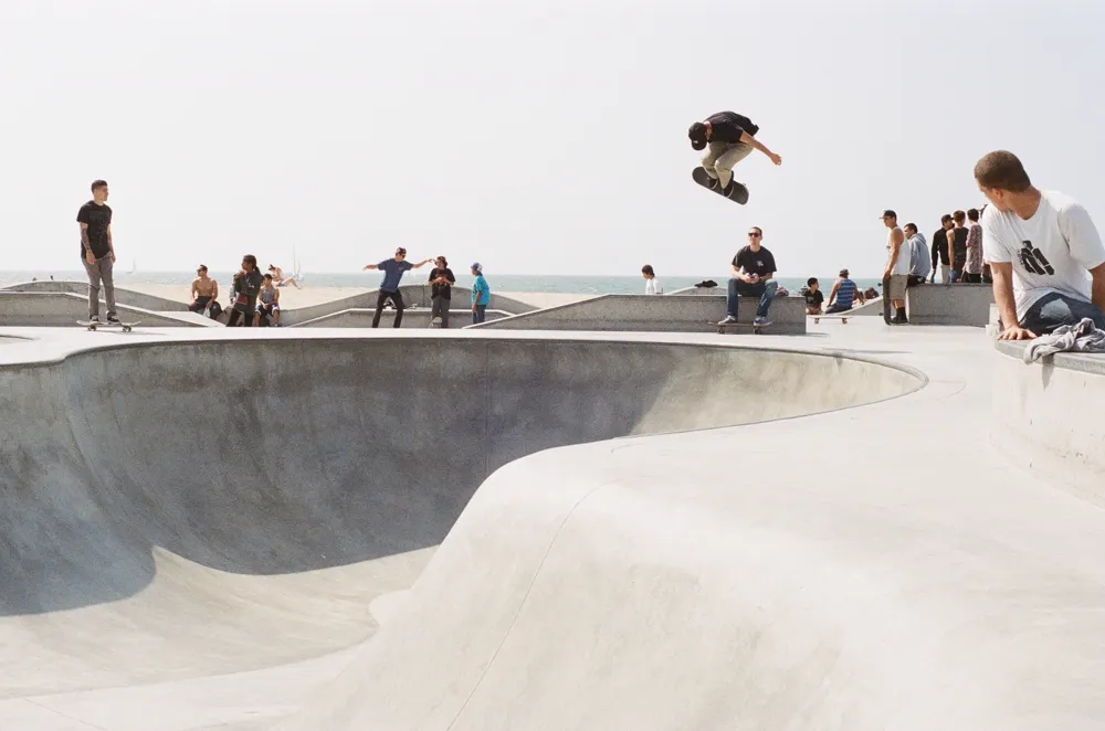 Skateboarder catching air over a seaside concrete skatepark bowl while other skaters watch, illustrating skateboarding content on Instagram in the US