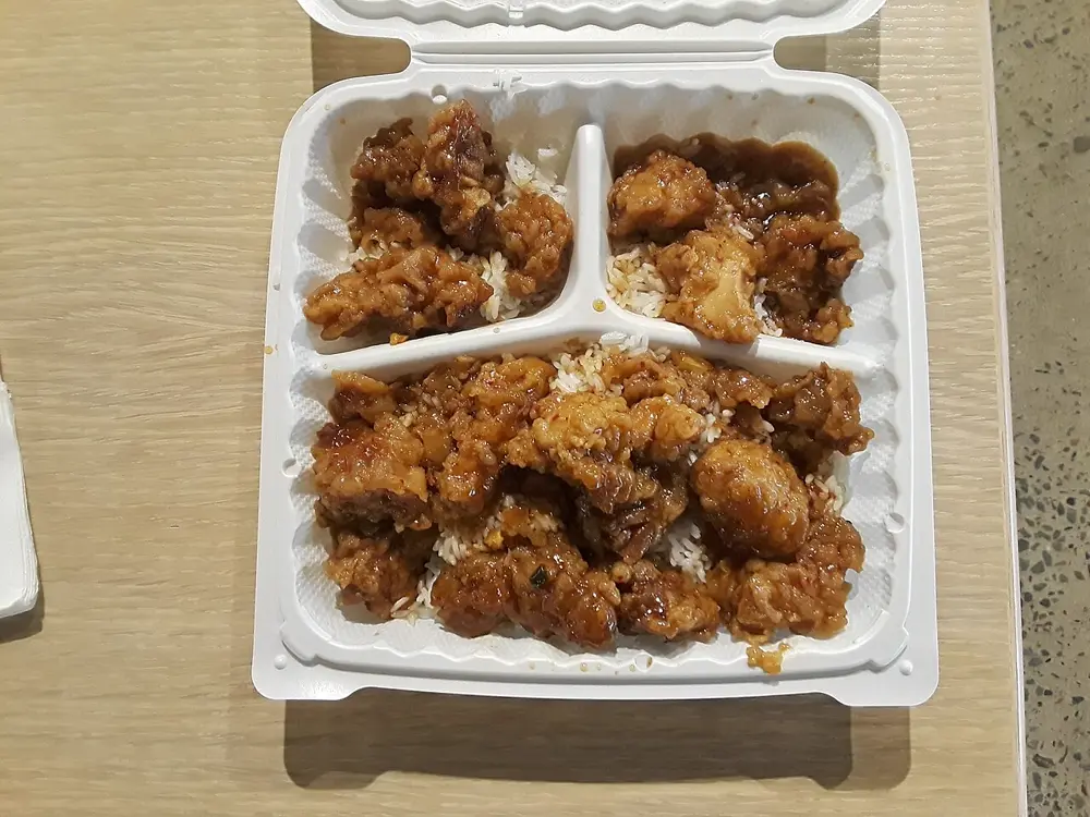 Orange chicken over white rice in an open takeout container, the kind of home-cooked order featured in food mukbang videos on Instagram in the US