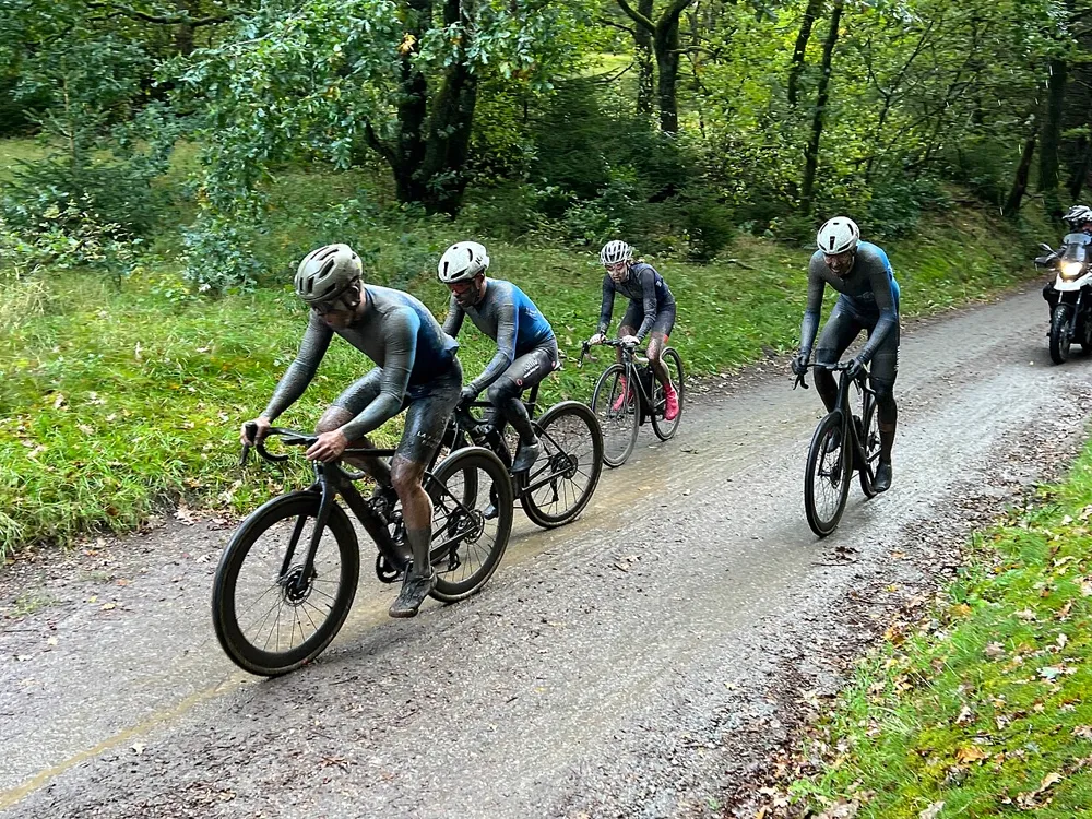 Group of gravel cyclists racing on a muddy forest road, illustrating gravel racing content on Instagram