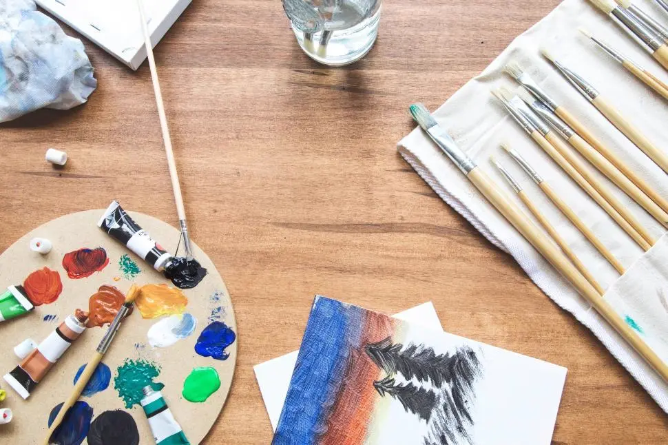 Paint palette, brushes and a small canvas on a wooden table, illustrating art content on Instagram in the US